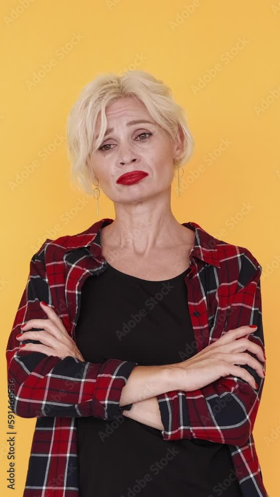 Vertical video. Disappointing situation. Sad woman. Regretful feelings. Upset middle-aged lady expressing sorrow crossing hands on chest on yellow. Vertical video. Disappointing situation. Sad woman. Regretful feelings. Upset middle-aged lady expressing sorrow crossing hands on chest on yellow.