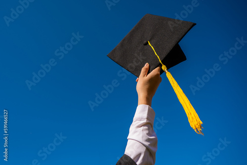 Close-up of a woman's hand with a graduation cap against the blue sky.  photo