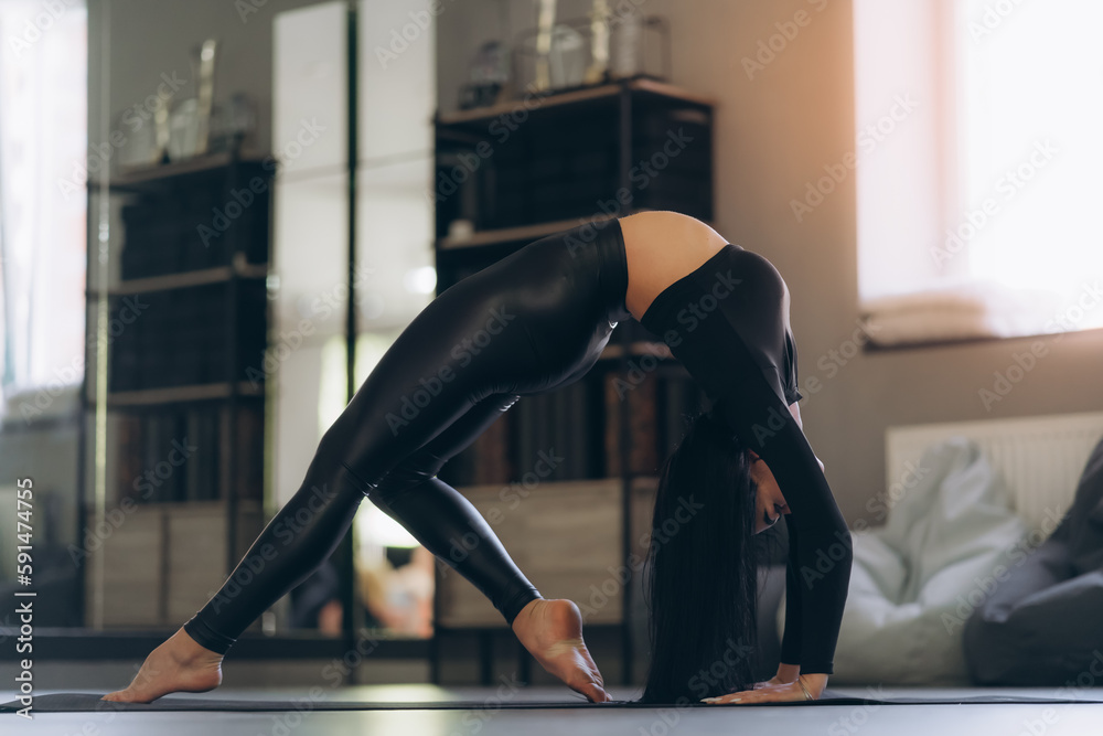 A woman in black sportswear, on the floor, on a mat, practicing the bridge asana in a bright room, helps relieve back pain, a flexible body stretch for beginners.