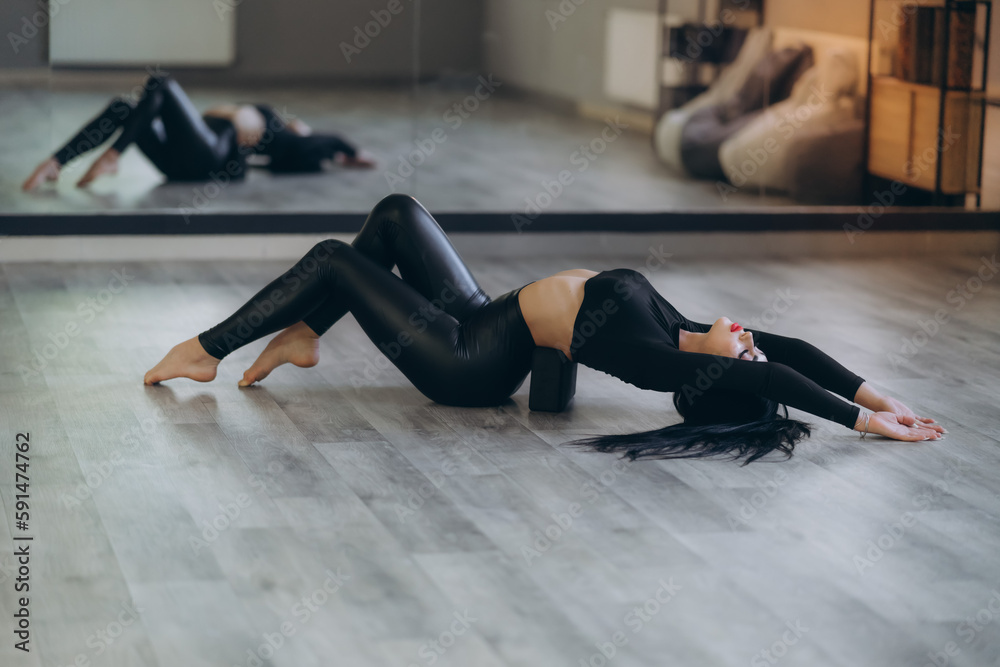 sports girl on the floor on a stretching block, back exercise, in a bright room, helps relieve back pain, flexible body stretching for beginners.