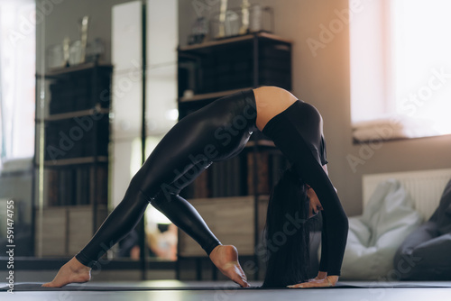 A woman in black sportswear, on the floor, on a mat, practicing the bridge asana in a bright room, helps relieve back pain, a flexible body stretch for beginners.