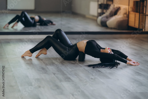 sports girl on the floor on a stretching block, back exercise, in a bright room, helps relieve back pain, flexible body stretching for beginners.