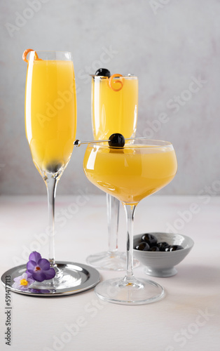 Three mimosa cocktails in a mix of glasses with orange twist and cocktail cherry garnishes, a bowl of cherries, cocktail pick and crocus blossoms.