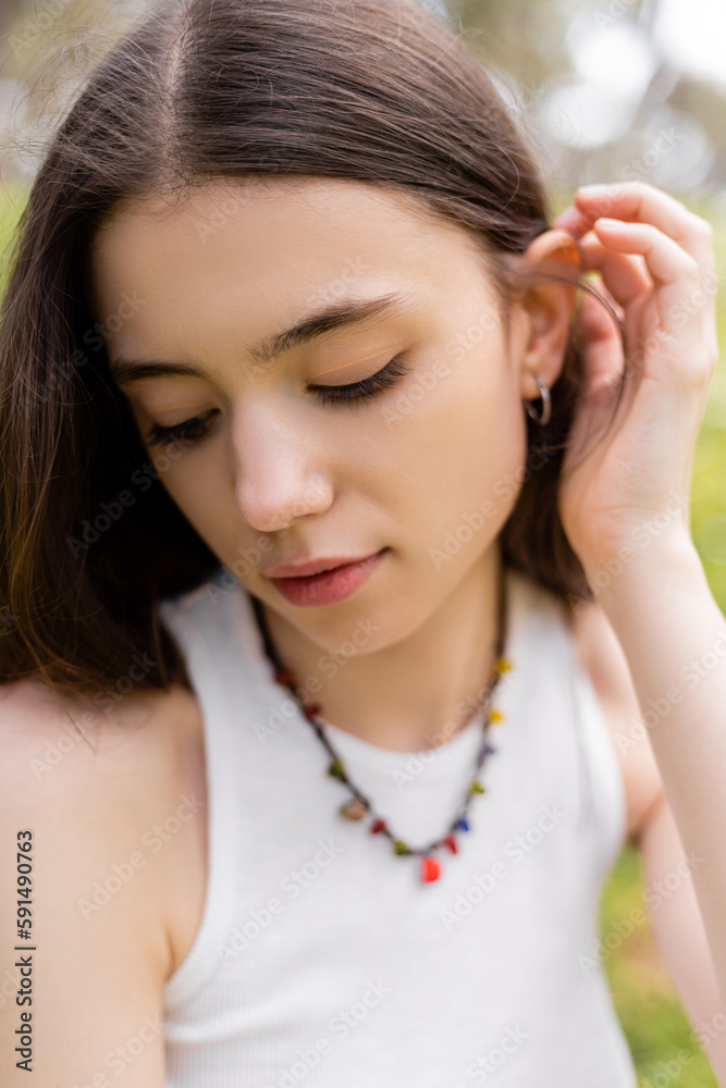 Fototapeta premium Portrait of young woman in top touching brunette hair outdoors.