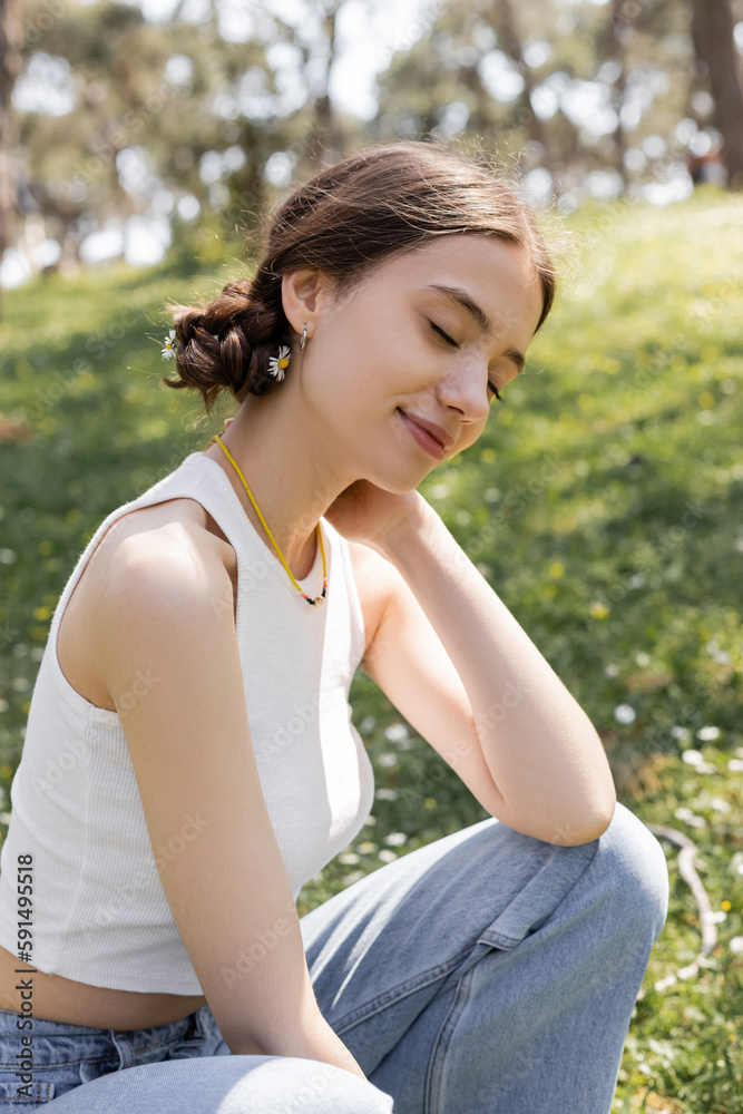 Overjoyed young woman with flowers in hair sitting on blurred lawn in summer park. Overjoyed young woman with flowers in hair sitting on blurred lawn in summer park.
