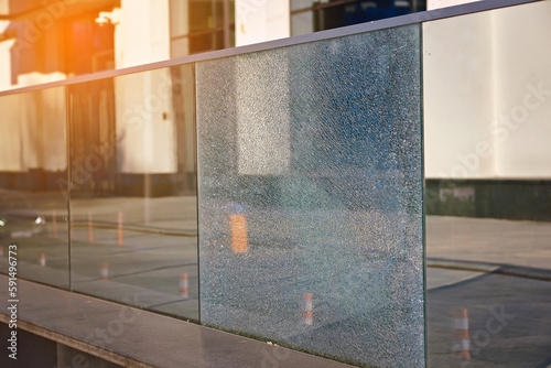Damaged tempered glass fence. Broken glass fence with banisters. Broken guard rail on office terrace. Steel railing with damaged panel, cracks on broken tempered glass. Fencing repair