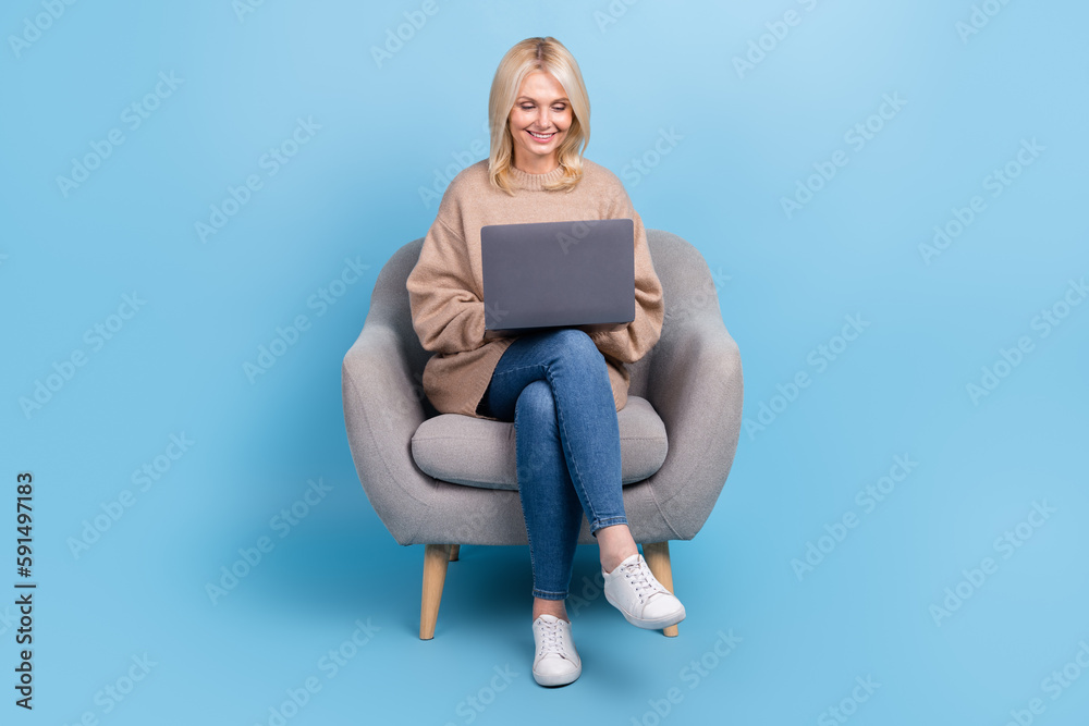 Full body cadre of satisfied it company team leader retired lady sitting armchair hold laptop coworking isolated on blue color background Full body cadre of satisfied it company team leader retired lady sitting armchair hold laptop coworking isolated on blue color background