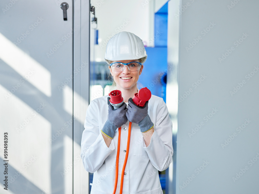 Happy woman wearing lab coat analyzing power plug in laboratory Happy woman wearing lab coat analyzing power plug in laboratory