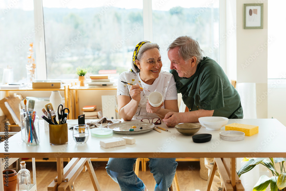 Happy senior man with woman painting ceramic cup in workshop Happy senior man with woman painting ceramic cup in workshop