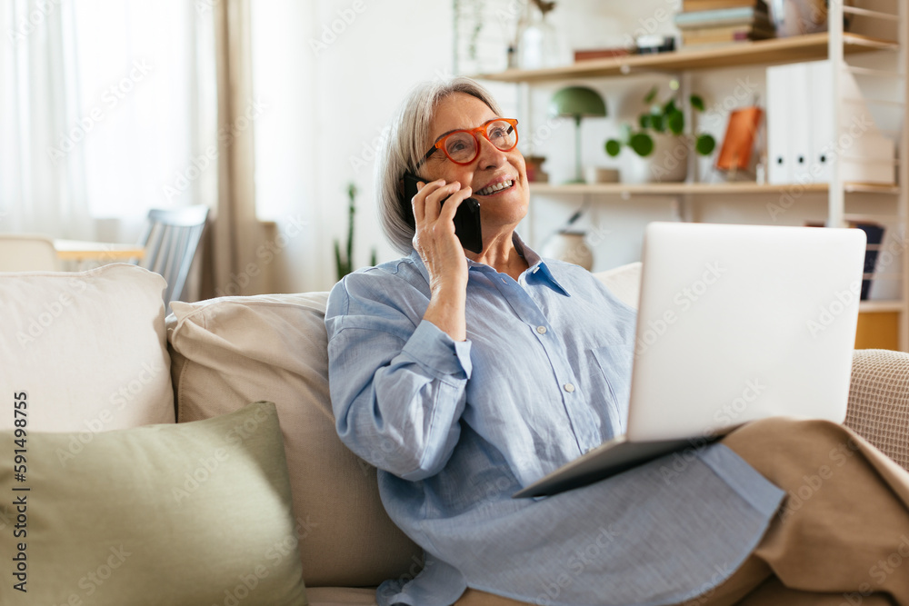 Smiling woman talking on smart phone sitting with laptop in living room Smiling woman talking on smart phone sitting with laptop in living room