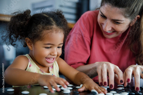 Happy mother and daughter playing go game at home photo