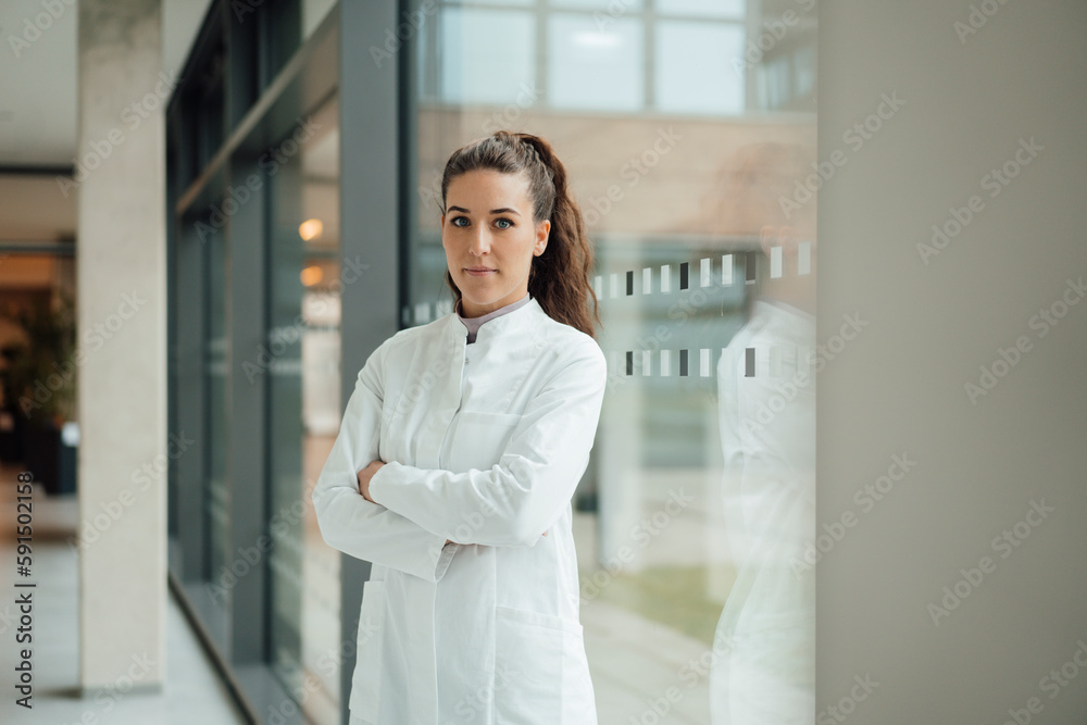 Confident woman in lab coat standing with crossed arms near window Confident woman in lab coat standing with crossed arms near window