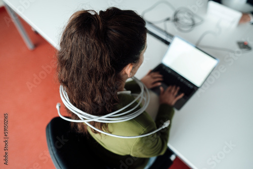 Businesswoman working on laptop tied up in cable at office photo