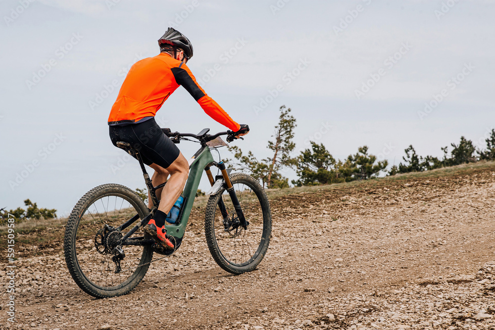 Obraz premium male cyclist riding mountain bike uphill cross-country cycling, biking on gravel road