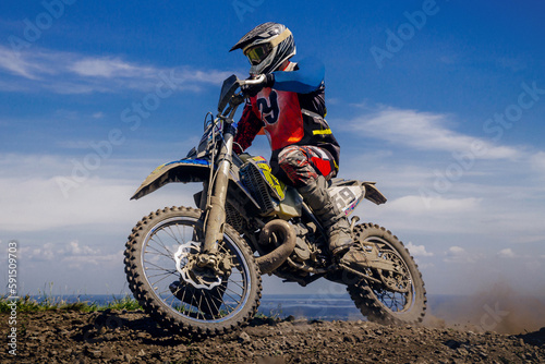 close-up motocross rider riding off-road motorcycle racing dusty trail on background blue sky