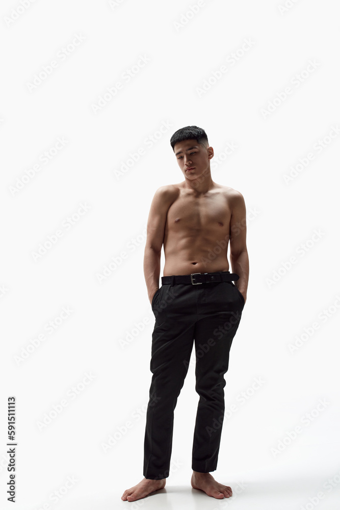 Fototapeta premium Full-length portrait of handsome young man with fit, attractive, muscular body posing shirtless in trousers against white studio background. Concept of male beauty, skincare, cosmetology, men's health
