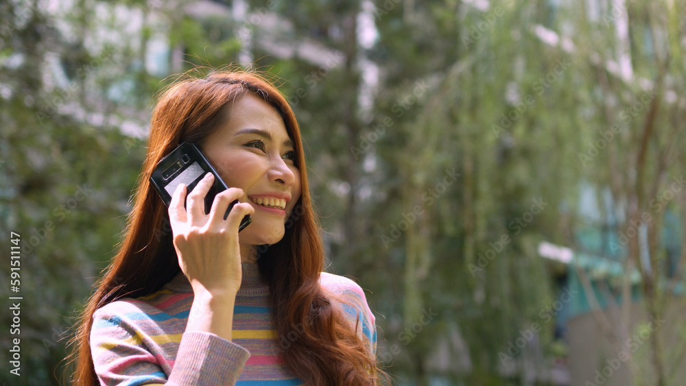 A smiling female tourist talking via smartphone on the park in the hotel. Feel happy. Close up happy woman chatting on mobile phone outdoor. A smiling female tourist talking via smartphone on the park in the hotel. Feel happy. Close up happy woman chatting on mobile phone outdoor.