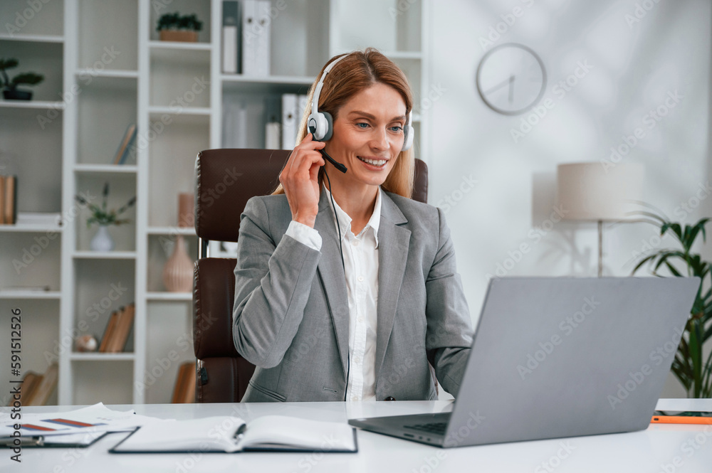 In headphones, by laptop, call center. Woman in business formal clothes is working in office In headphones, by laptop, call center. Woman in business formal clothes is working in office