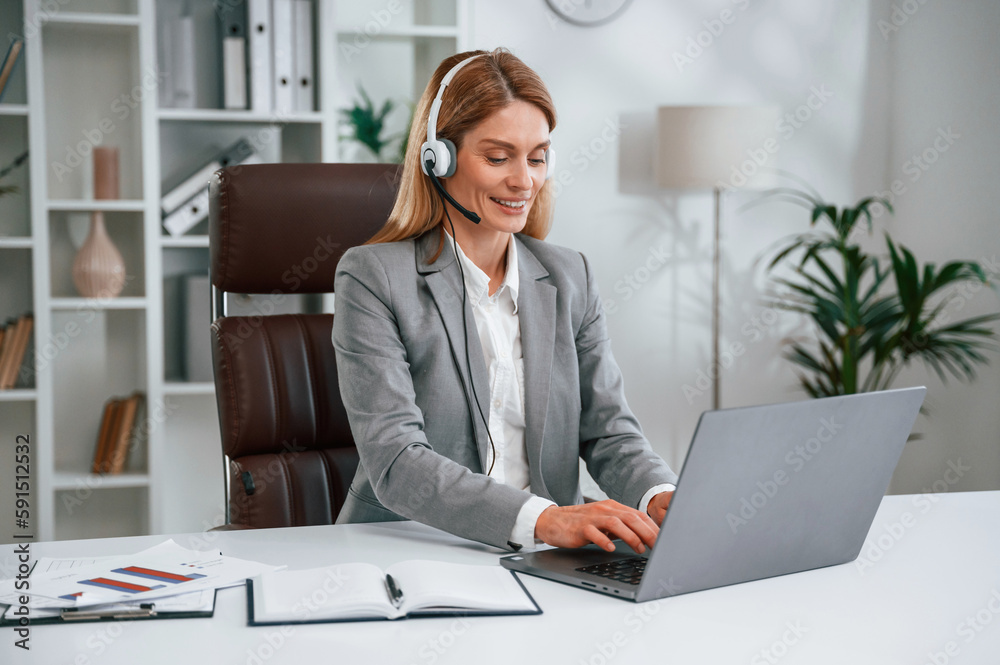 In the call center. In headphones. Woman in business formal clothes is working in office In the call center. In headphones. Woman in business formal clothes is working in office