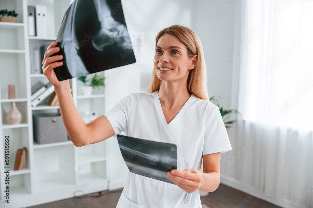 Checking x-ray. Young female doctor in white coat is indoors Checking x-ray. Young female doctor in white coat is indoors