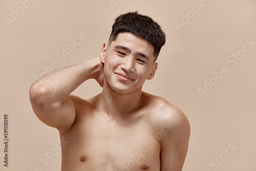 Morning routine. Handsome, cute, young asian guy with clear, spotless face posing shirtless against light brown studio background. Concept of male beauty, skincare, cosmetology, men's health