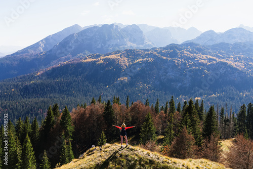 Top view of a female tourist who stands on a trail against the background of a forest and a mountain range