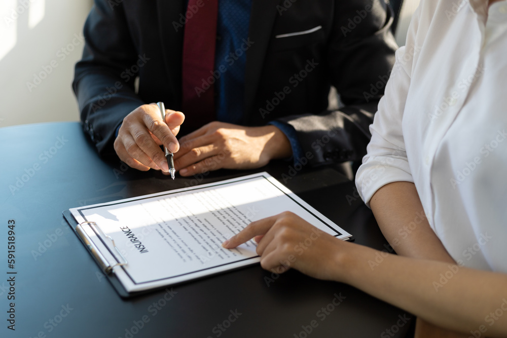 Businessman in suit in his office showing home insurance policy and pointing with a pen where the policyholder must to sign. Insurance agent consulting real estate insurance detail to customer. Businessman in suit in his office showing home insurance policy and pointing with a pen where the policyholder must to sign. Insurance agent consulting real estate insurance detail to customer.