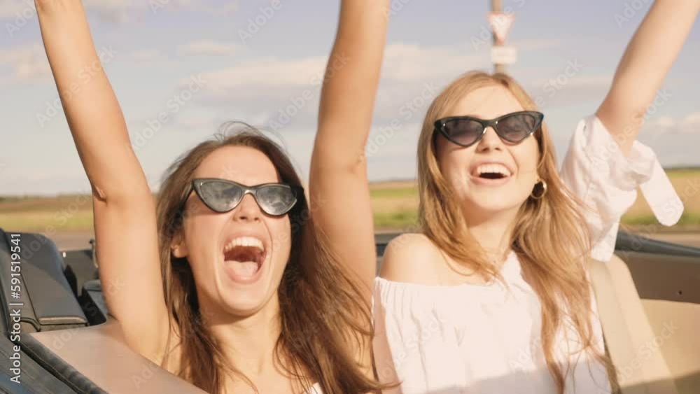 Portrait of two young beautiful and smiling hipster female in convertible car. Sexy carefree women driving. Positive models riding and having fun, enjoying summer days
