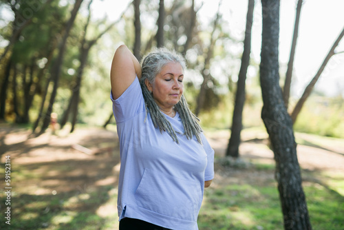 Mature elderly grey haired dreadlocks woman training in park, doing yoga or fitness - wellbeing and healthy lifestyle concept © satura_