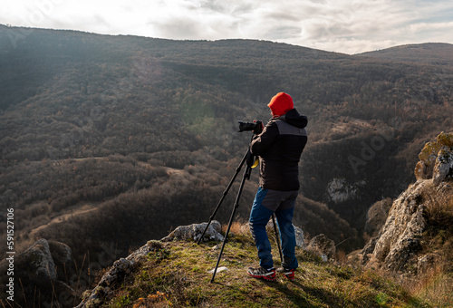 Photographer taking photographs with digital camera on a tripod in mountains. Travel and active lifestyle concept