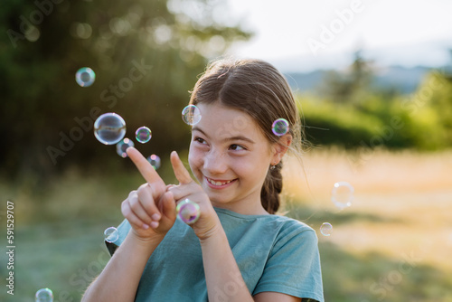Portrait of a beautiful little girl smiling in nature  with bubbles in the background.