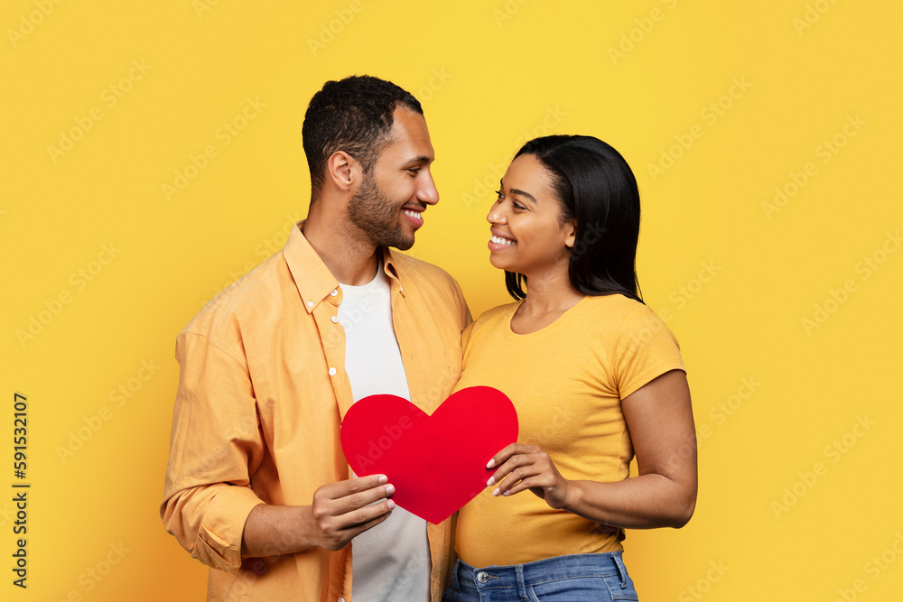 Cheerful millennial african american guy and lady hold heart, enjoy love Cheerful millennial african american guy and lady hold heart, enjoy love
