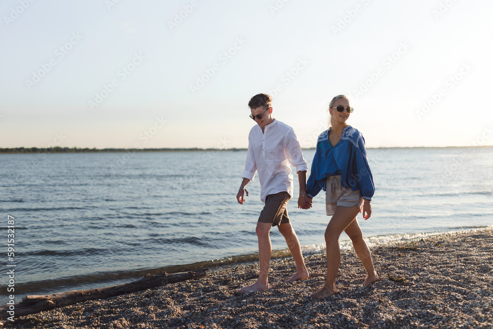 Happy young couple walking on the beach during sunset, prepairing for picnic.