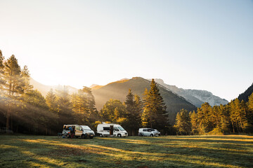 Camper vans in a valley with amazing landscape views of forest, mountains and sun rays during sunrise. Van road trip holiday and outdoor summer adventure. Nomad lifestyle concept