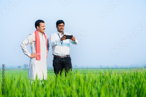 Photography banker or officer with farmer taking crop photos for growth analysis on mobile phone at farmland - concept of technology, modern farming and examines paddy plantation