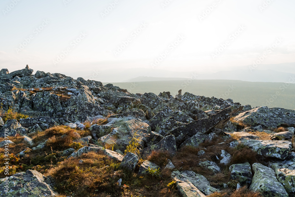 Dawn in the mountains, large kurum stones on the slope of the peak, moss grows on the stones, juniper bushes, sunlight, glare of the sun. Dawn in the mountains, large kurum stones on the slope of the peak, moss grows on the stones, juniper bushes, sunlight, glare of the sun.