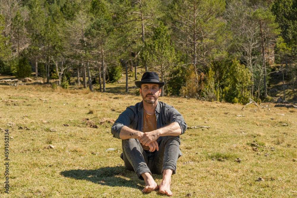 man sitting barefoot on mountain with hat, enjoying good weather, landscape
