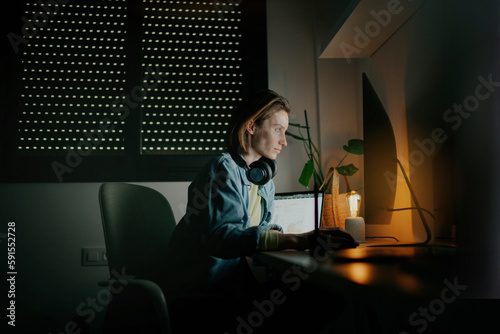 A woman sitting at her desk, either in a cozy office or at home, intently focused on her computer screen while working at night. relaxed and focused
