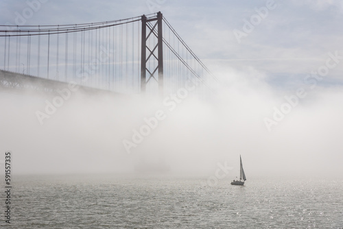 Suspension bridge shrouded in white fog - sailboat sails the sea