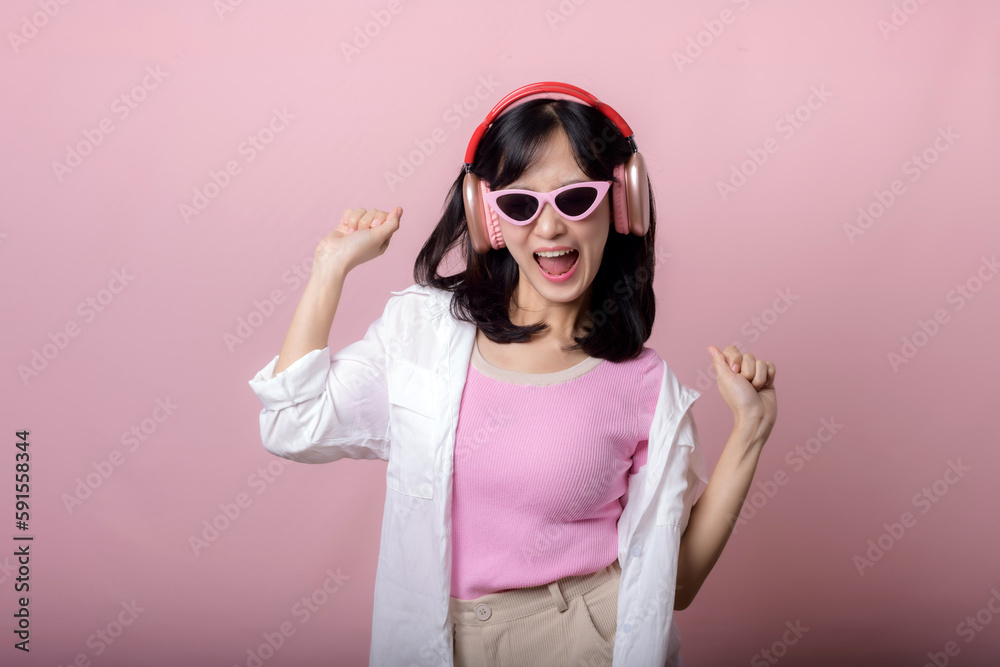 happy young asian woman model with stylish trendy sun glasses enjoy listening music by headphone audio and dancing isolated on pink studio background. technology, girl fashion, accessory concept. happy young asian woman model with stylish trendy sun glasses enjoy listening music by headphone audio and dancing isolated on pink studio background. technology, girl fashion, accessory concept.