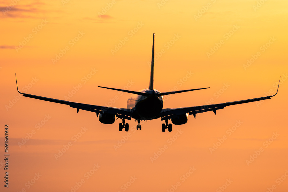 Silhouette of airplane in flight against orange sunset sky