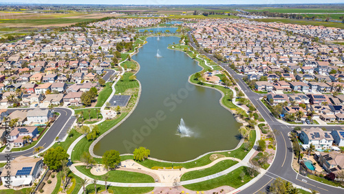 Drone photos over The Lakes community in Discovery Bay, California with houses, houses with solar, a lake with fountains, roadways and a beautiful blue sky with room for text