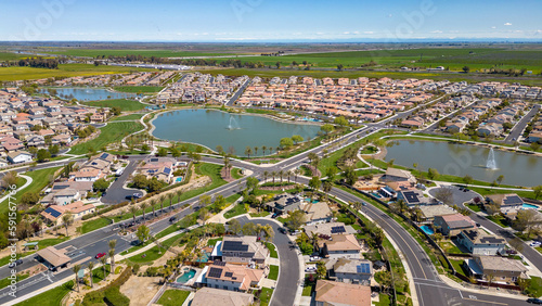 Drone photos over The Lakes community in Discovery Bay, California with houses, houses with solar, a lake with fountains, roadways and a beautiful blue sky with room for text