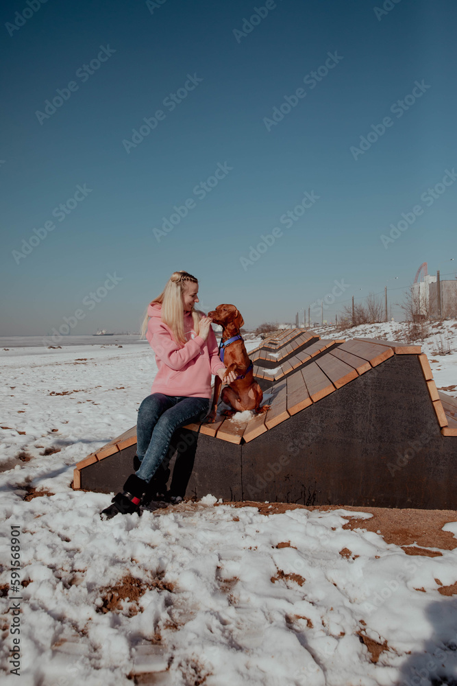 Girl in pink jacket sits with a dog on a bench in winter