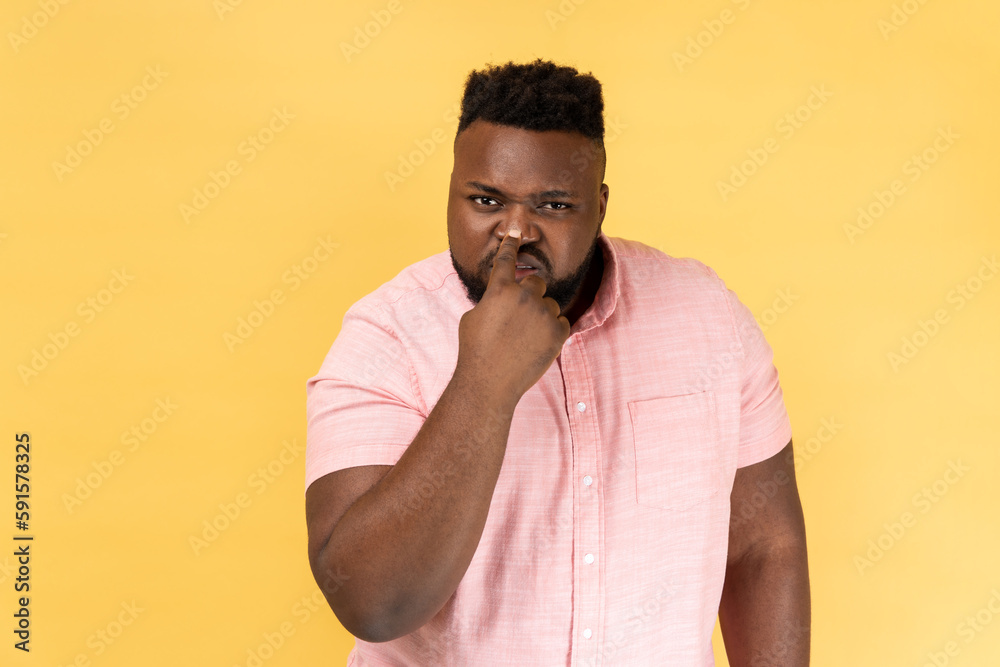 This is lie. Portrait of suspicious man wearing pink shirt touching nose, doing liar gesture, body language symbol of cheats, falsehood and deception. Indoor studio shot isolated on yellow background.