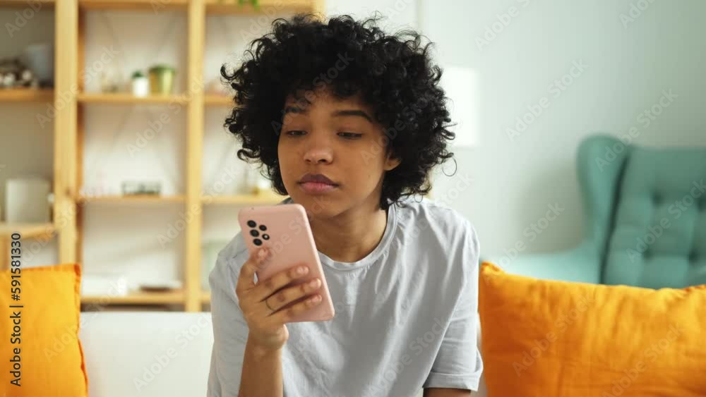 Excited happy young black african american woman holding cell phone laughing feeling joy getting mobile message. Overjoyed girl laughing aloud sitting on couch watching funny video reading news Excited happy young black african american woman holding cell phone laughing feeling joy getting mobile message. Overjoyed girl laughing aloud sitting on couch watching funny video reading news