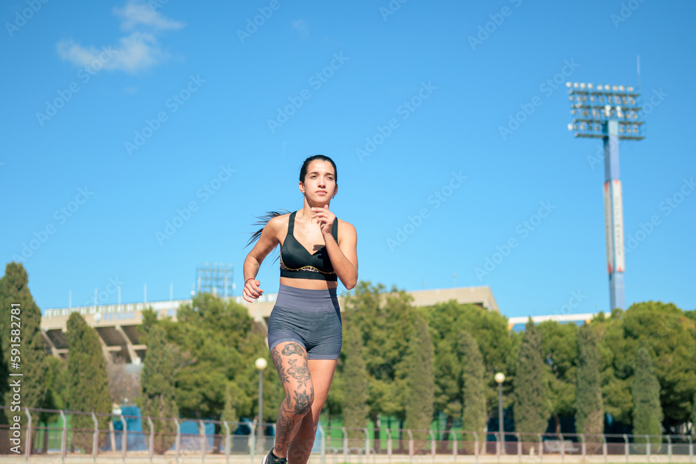 Woman with tattoos running on athletic track on a sunny day