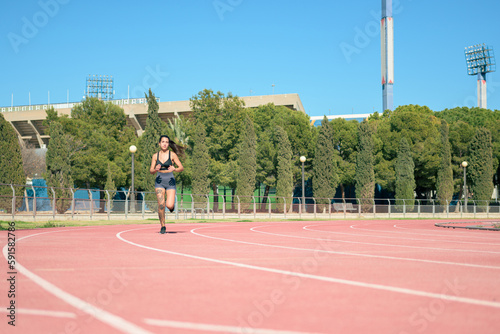 Woman with tattoos running on athletic track on a sunny day