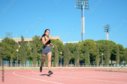 Woman with tattoos running on athletic track on a sunny day