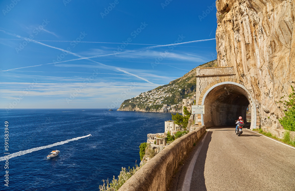 Fototapeta premium Scooter drives along the road along the Amalfi coast, approaching the tunnel Conca dei Marini